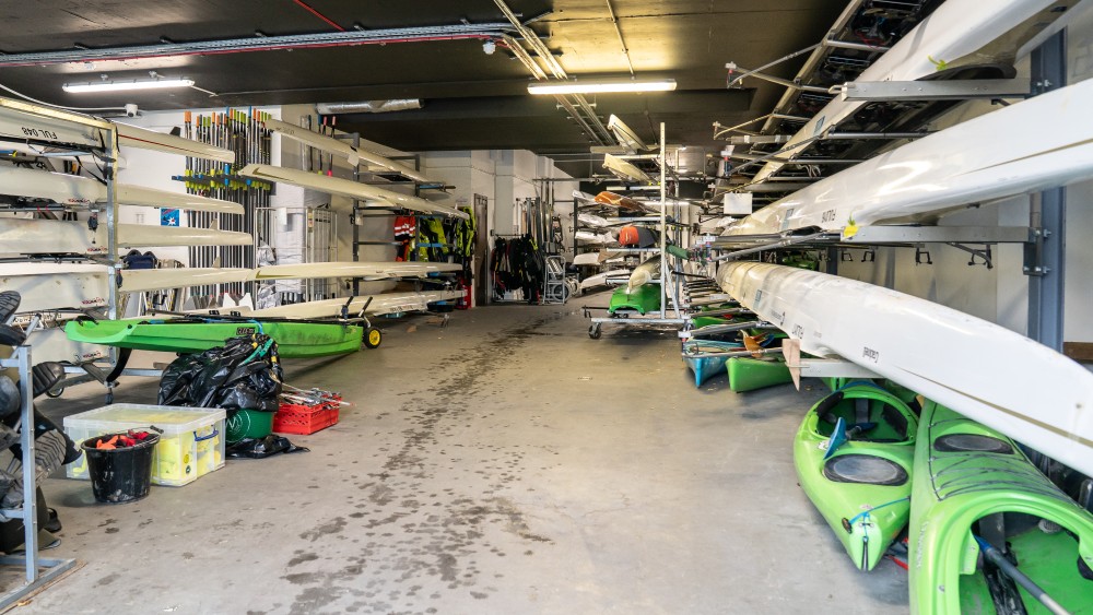 Canoes and kayaks hang from racks on walls inside a container.