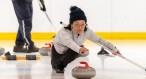 A woman releases a curling stone while crouched down on the ice.